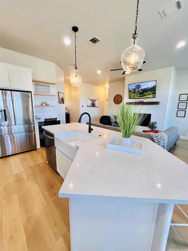 kitchen with stainless steel refrigerator with ice dispenser, visible vents, open floor plan, an island with sink, and light wood-type flooring