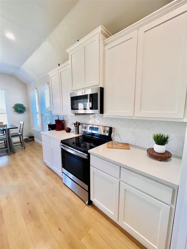 kitchen featuring white cabinets, vaulted ceiling, appliances with stainless steel finishes, light wood-type flooring, and decorative backsplash