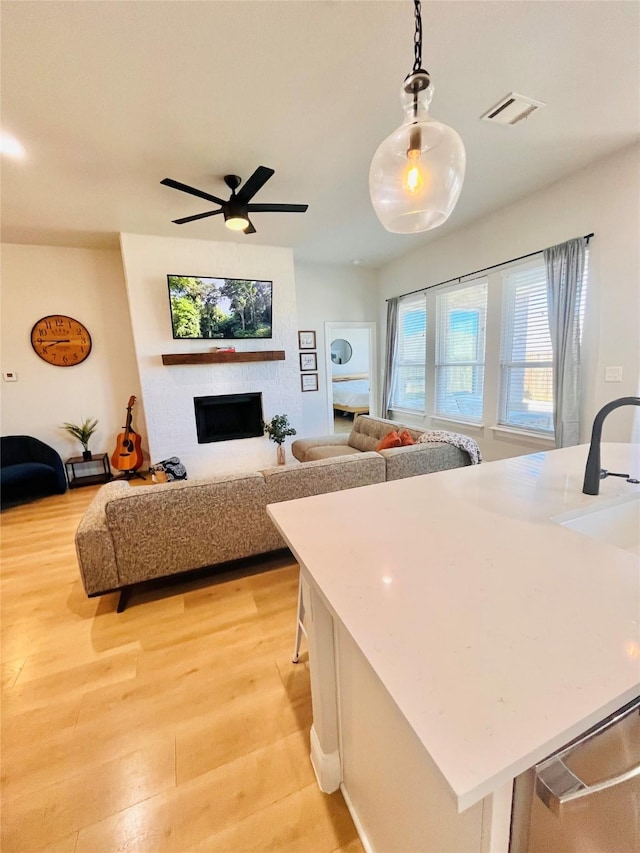 kitchen with a large fireplace, visible vents, open floor plan, hanging light fixtures, and light wood-type flooring