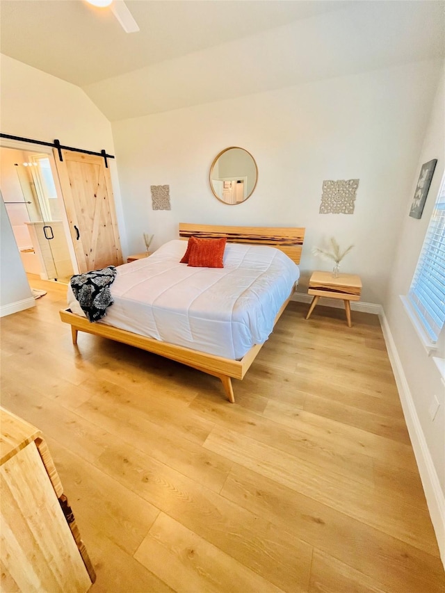 bedroom featuring lofted ceiling, light wood-style floors, a barn door, and baseboards