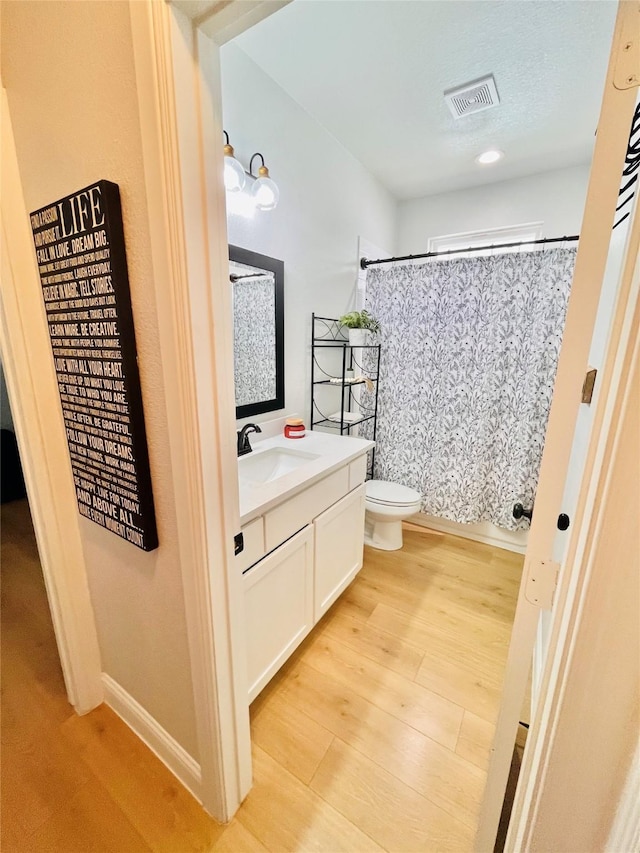 bathroom featuring visible vents, toilet, vanity, wood finished floors, and a shower with curtain