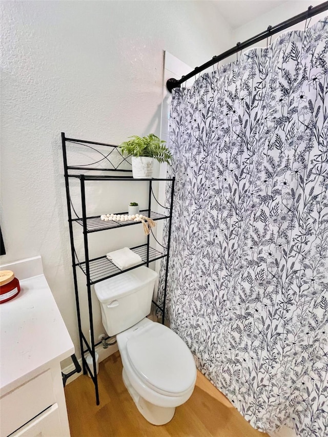 bathroom featuring a textured wall, toilet, a shower with curtain, wood finished floors, and vanity