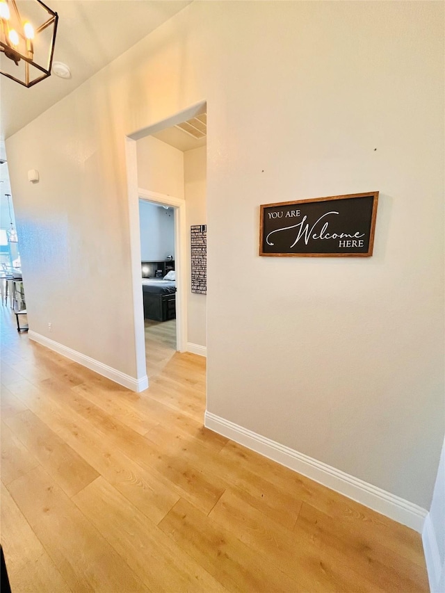 hallway with light wood-style flooring, a chandelier, and baseboards