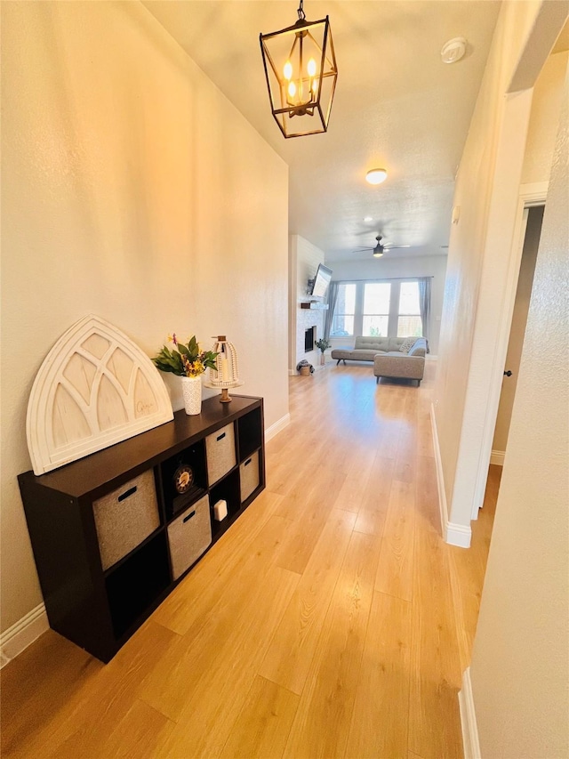 hall featuring light wood-style floors, baseboards, and a chandelier