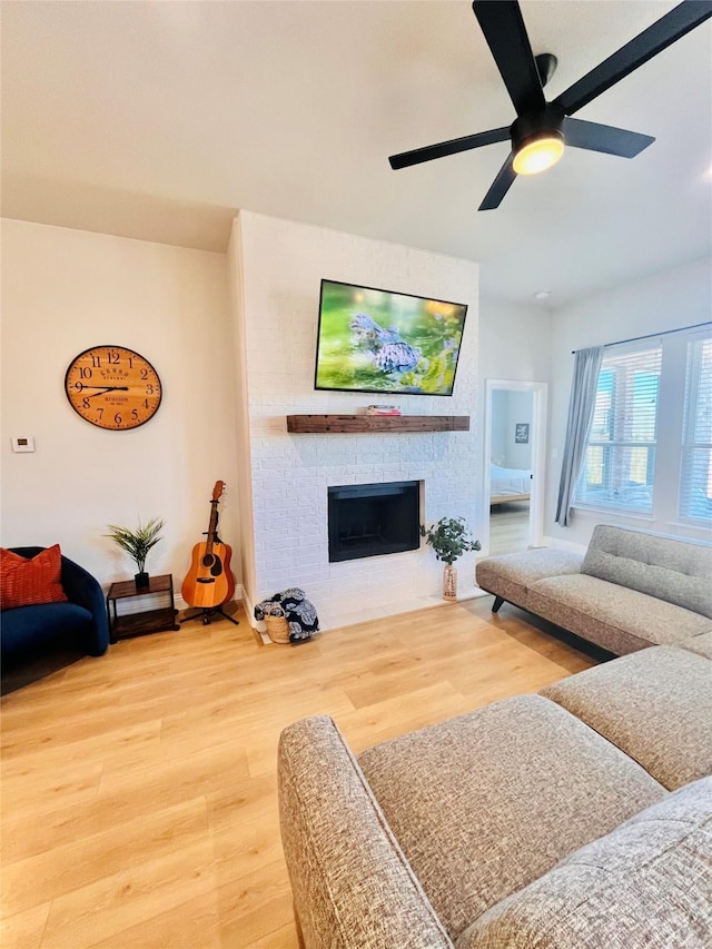 living room with a large fireplace, a ceiling fan, and wood finished floors