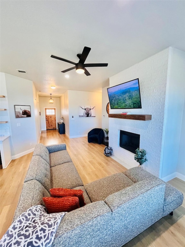 living area with a fireplace, visible vents, ceiling fan, wood finished floors, and baseboards