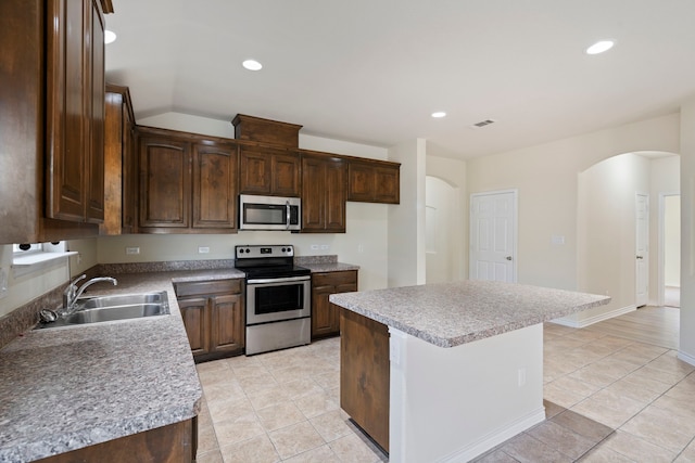 kitchen with arched walkways, appliances with stainless steel finishes, a center island, a sink, and recessed lighting