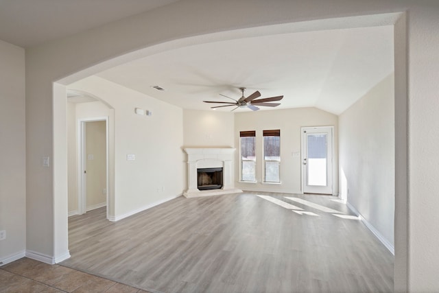 unfurnished living room featuring arched walkways, a fireplace with raised hearth, wood finished floors, visible vents, and a ceiling fan