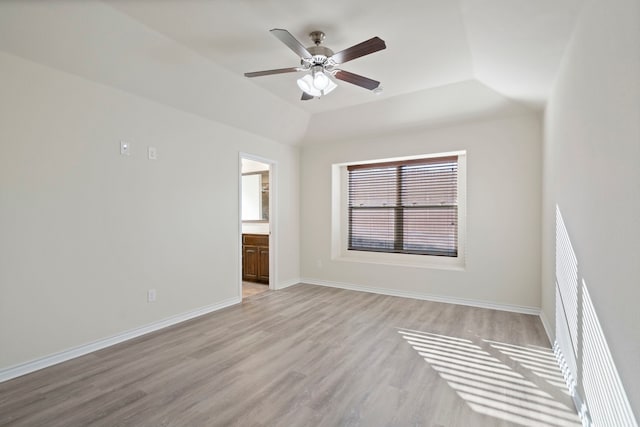 spare room featuring light wood finished floors, baseboards, vaulted ceiling, and a ceiling fan