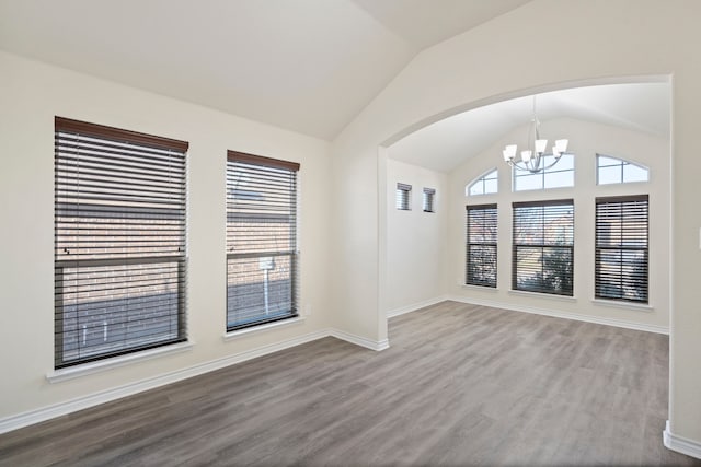 spare room with plenty of natural light, a chandelier, vaulted ceiling, and wood finished floors