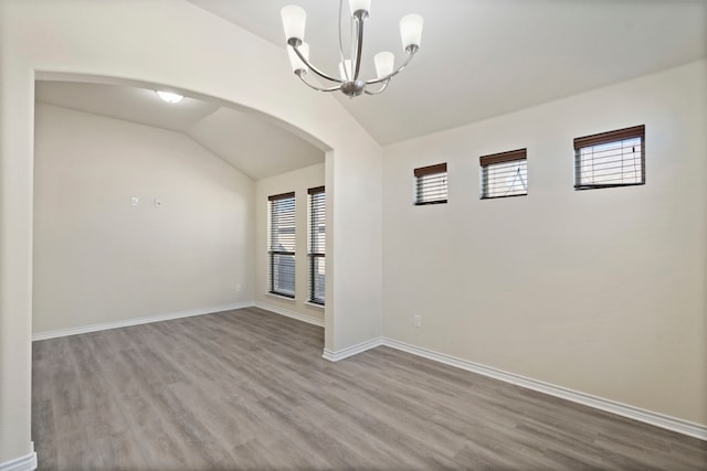 interior space with arched walkways, a chandelier, lofted ceiling, wood finished floors, and baseboards