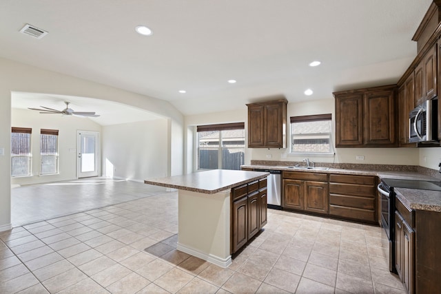 kitchen with stainless steel appliances, open floor plan, a sink, dark brown cabinetry, and a kitchen island