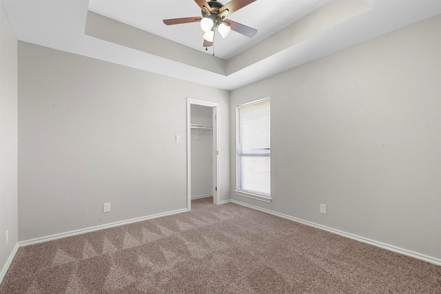 spare room featuring carpet, a tray ceiling, ceiling fan, and baseboards