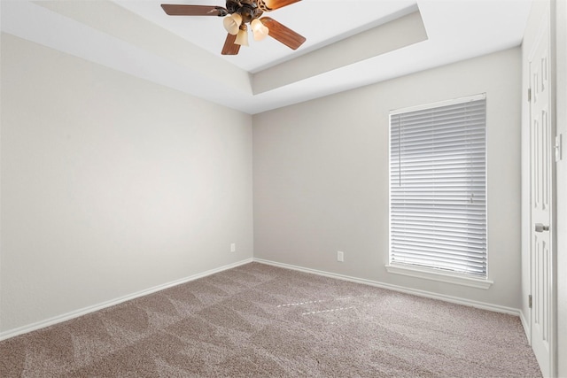 empty room with ceiling fan, carpet flooring, a raised ceiling, and baseboards