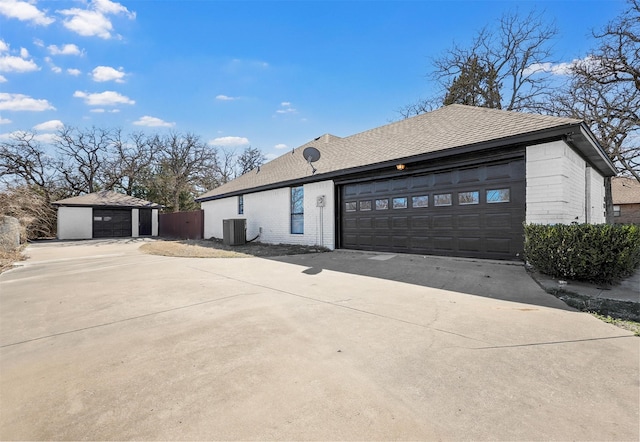 view of property exterior featuring a garage, brick siding, roof with shingles, and central air condition unit