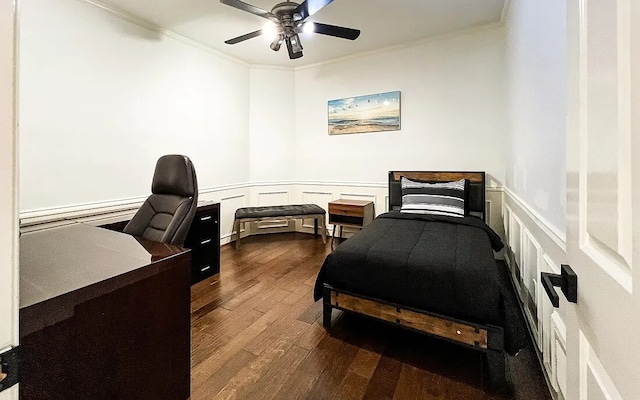 bedroom with a ceiling fan, dark wood-style floors, a wainscoted wall, ornamental molding, and a decorative wall