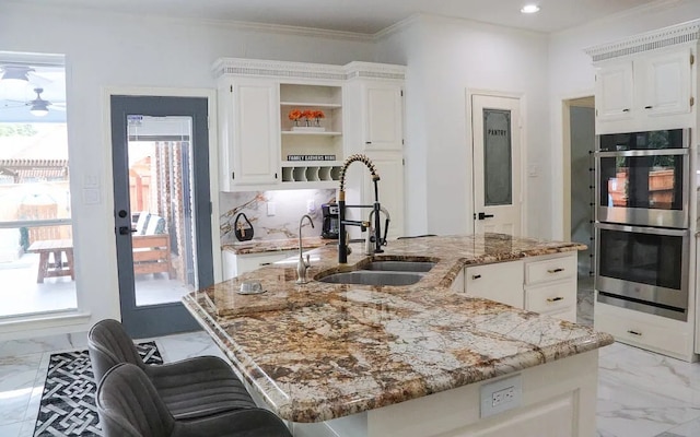 kitchen with a center island with sink, light stone counters, marble finish floor, stainless steel double oven, and a sink