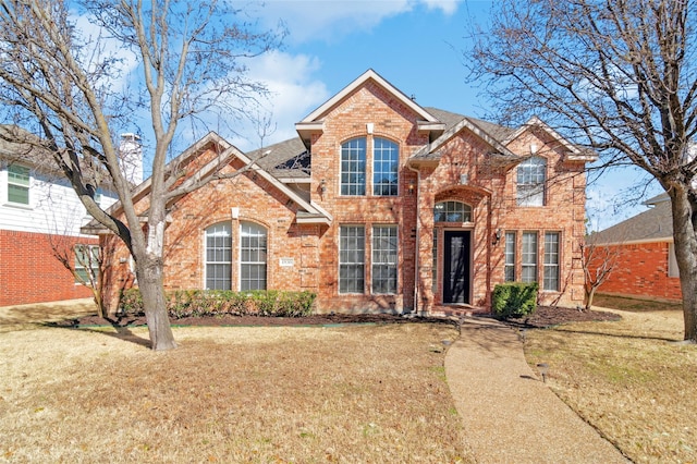 traditional-style home with brick siding, a front lawn, and a shingled roof