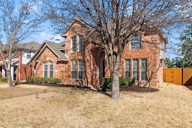 traditional home featuring brick siding, roof with shingles, a gate, fence, and a front lawn