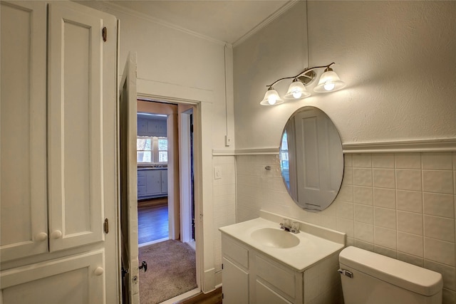 half bath featuring toilet, tile walls, vanity, wainscoting, and crown molding