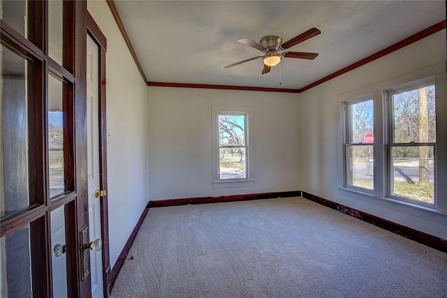 carpeted empty room with a ceiling fan, baseboards, and crown molding