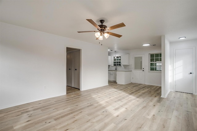 unfurnished living room featuring a ceiling fan, light wood-type flooring, a sink, and baseboards