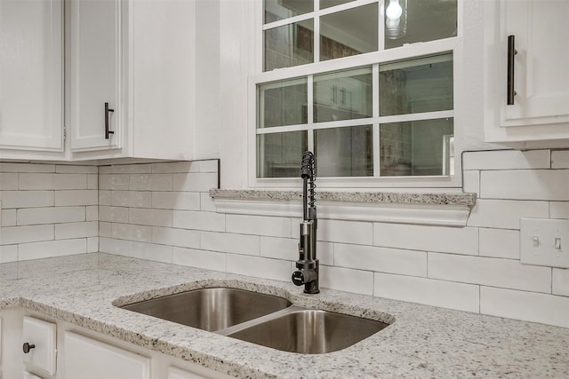 kitchen with tasteful backsplash, white cabinets, a sink, and light stone counters