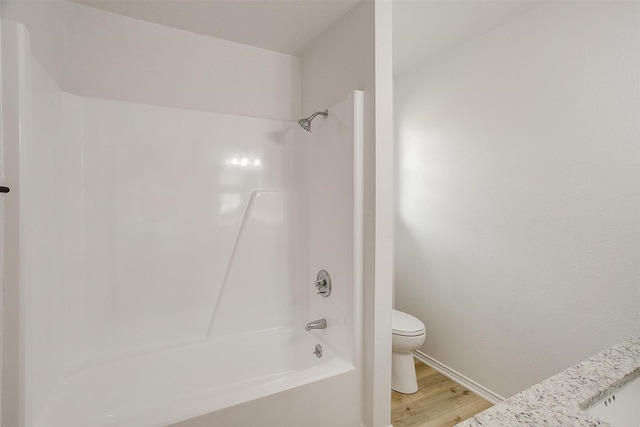 bathroom with washtub / shower combination, wood finished floors, and toilet