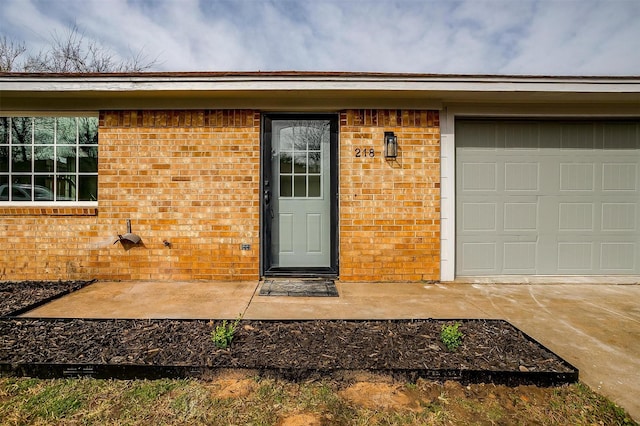 doorway to property with a garage, driveway, and brick siding