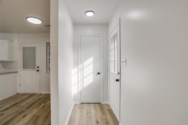 doorway with light wood finished floors, visible vents, and baseboards