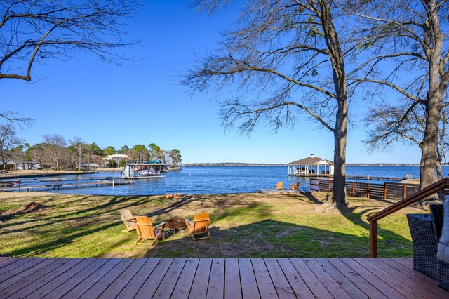 wooden deck with a water view, an outdoor fire pit, a lawn, and a boat dock