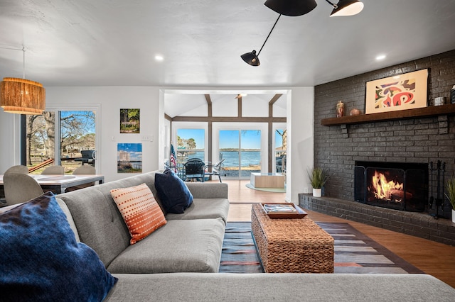 living room featuring wood finished floors, a brick fireplace, recessed lighting, and a water view