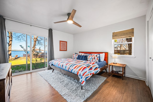 bedroom with baseboards, ceiling fan, wood finished floors, a water view, and access to exterior