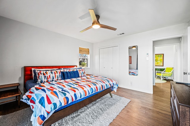 bedroom featuring ceiling fan, wood finished floors, visible vents, baseboards, and a closet