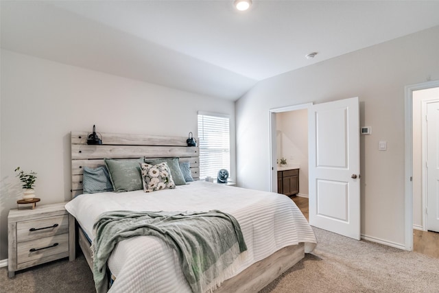 carpeted bedroom with ensuite bath, baseboards, and vaulted ceiling