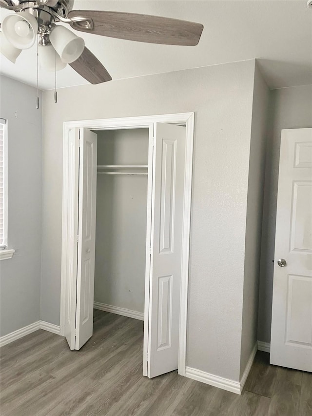 unfurnished bedroom with ceiling fan, a closet, wood finished floors, and baseboards