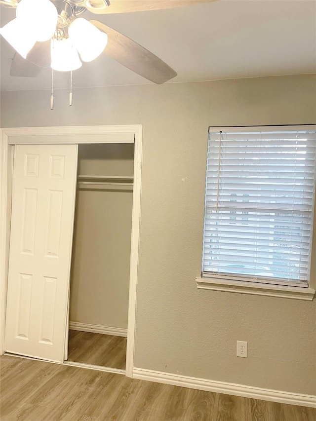 unfurnished bedroom featuring a ceiling fan, a closet, baseboards, and wood finished floors