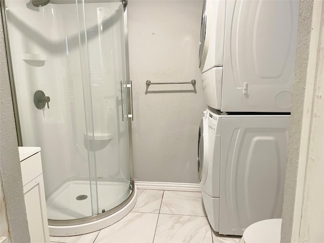 full bathroom with toilet, baseboards, marble finish floor, a stall shower, and stacked washer and clothes dryer