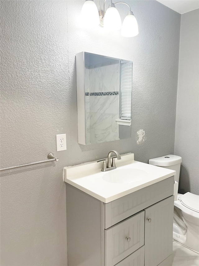 bathroom with a textured wall, vanity, and toilet