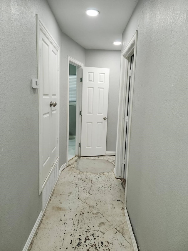 hall featuring concrete floors, baseboards, and a textured wall