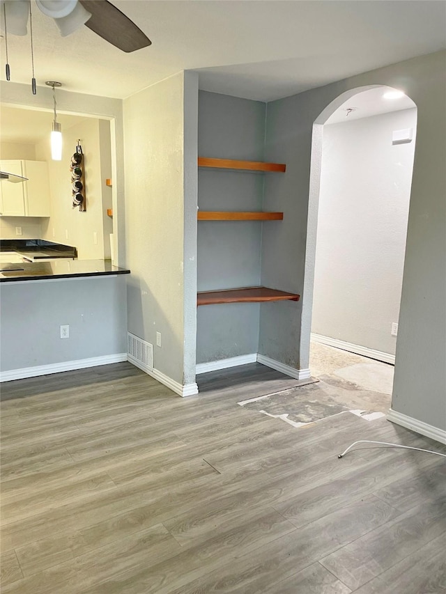 unfurnished living room with baseboards, visible vents, arched walkways, and wood finished floors