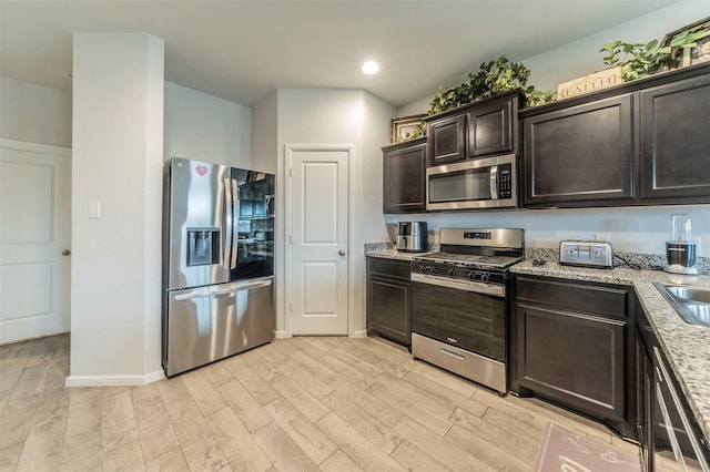 kitchen featuring dark brown cabinetry, stainless steel appliances, baseboards, light stone countertops, and light wood finished floors