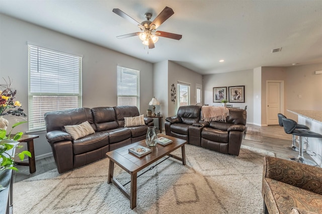 living area with light wood-style floors, visible vents, ceiling fan, and baseboards