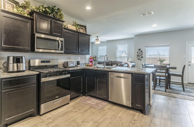 kitchen featuring light wood finished floors, visible vents, a peninsula, stainless steel appliances, and a sink