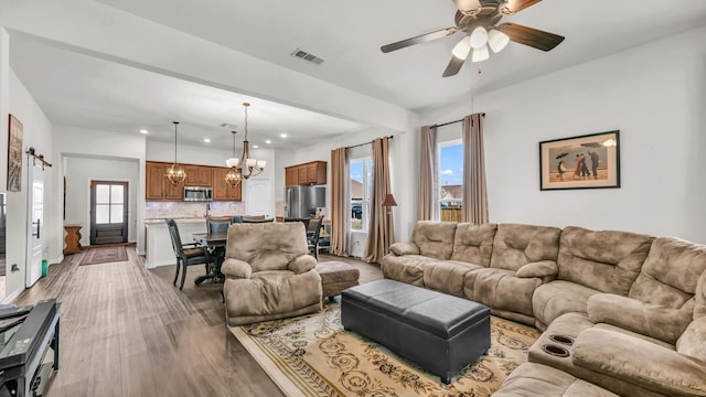 living area featuring light wood finished floors, a barn door, visible vents, ceiling fan with notable chandelier, and recessed lighting