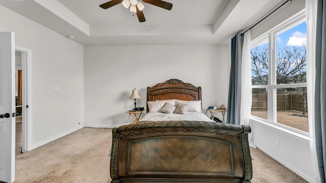 bedroom featuring a ceiling fan, a raised ceiling, light colored carpet, and baseboards