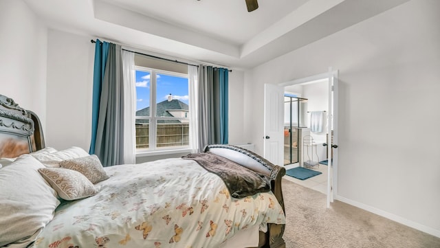 carpeted bedroom featuring a tray ceiling, a ceiling fan, and baseboards