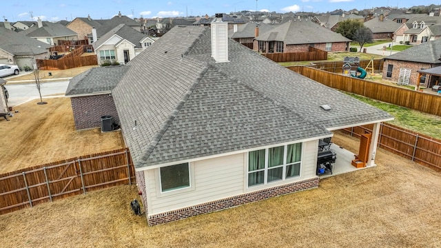 exterior space with a shingled roof, a chimney, a fenced backyard, and a residential view