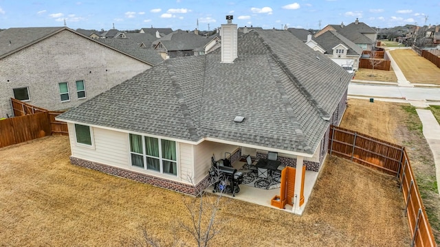 back of property with a shingled roof, a chimney, a fenced backyard, and a residential view