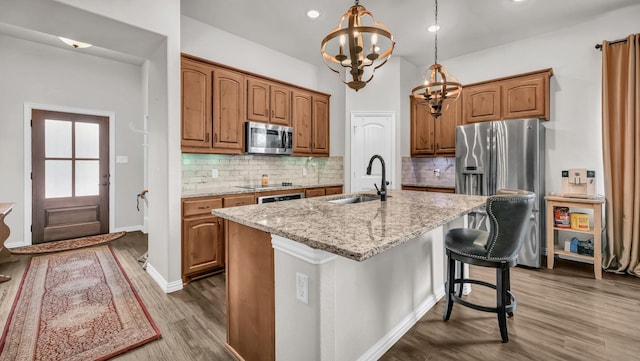 kitchen featuring dark wood finished floors, stainless steel microwave, light stone counters, a sink, and a notable chandelier